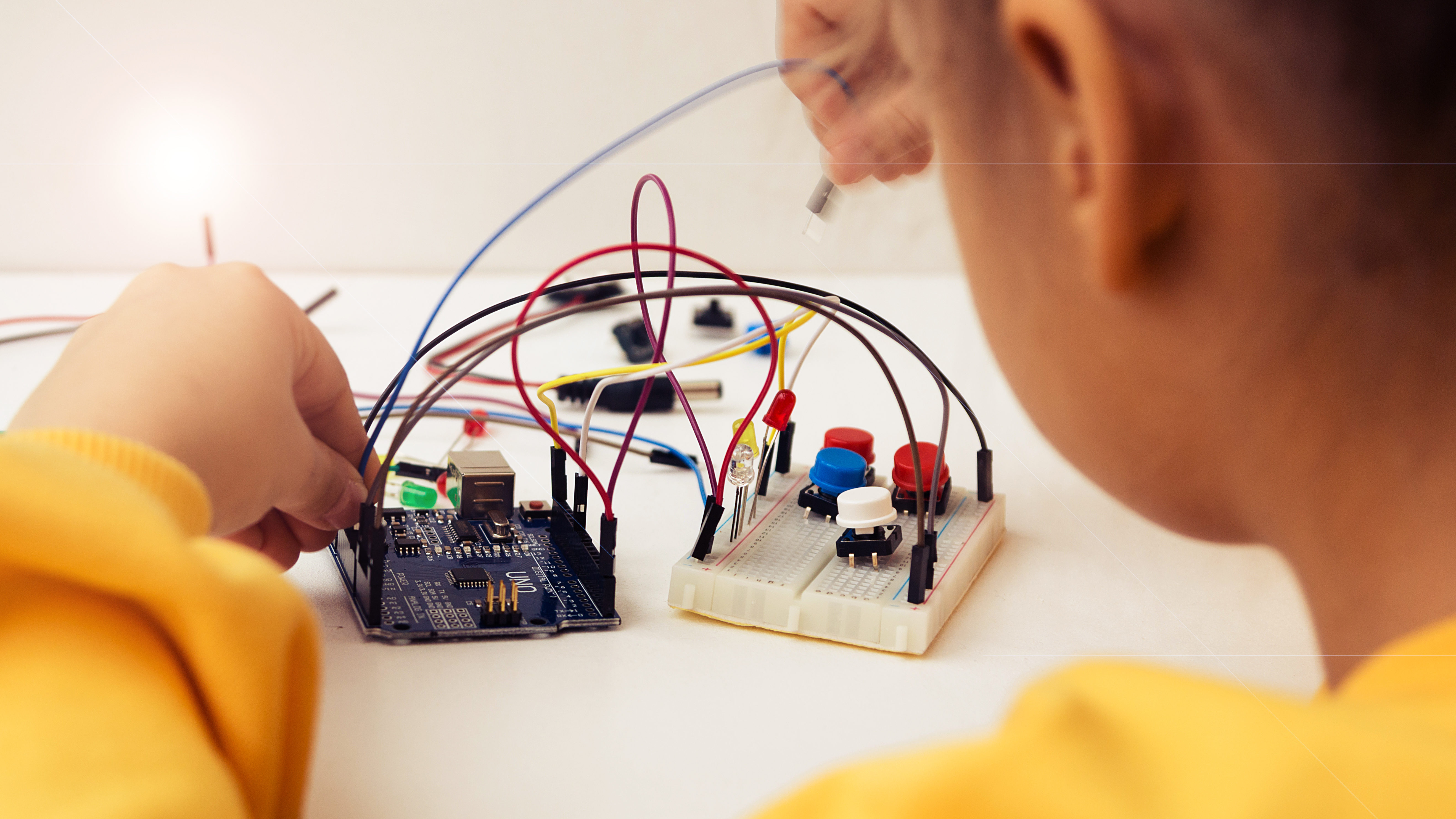 A child working on an electronics project using a breadboard and an Arduino Uno microcontroller, with various wires, LEDs, and buttons connected.