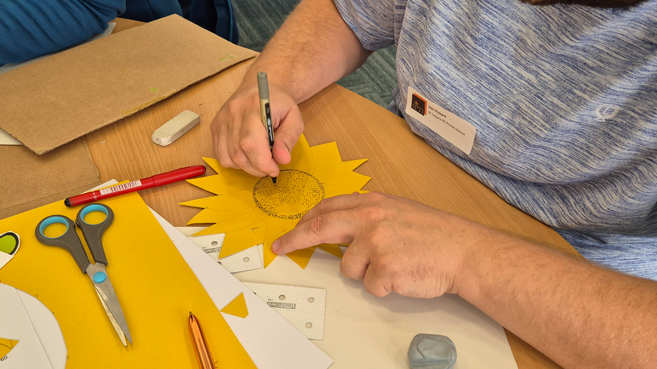 Teacher colouring in a sunflower with scissors and paper cuttings on the table