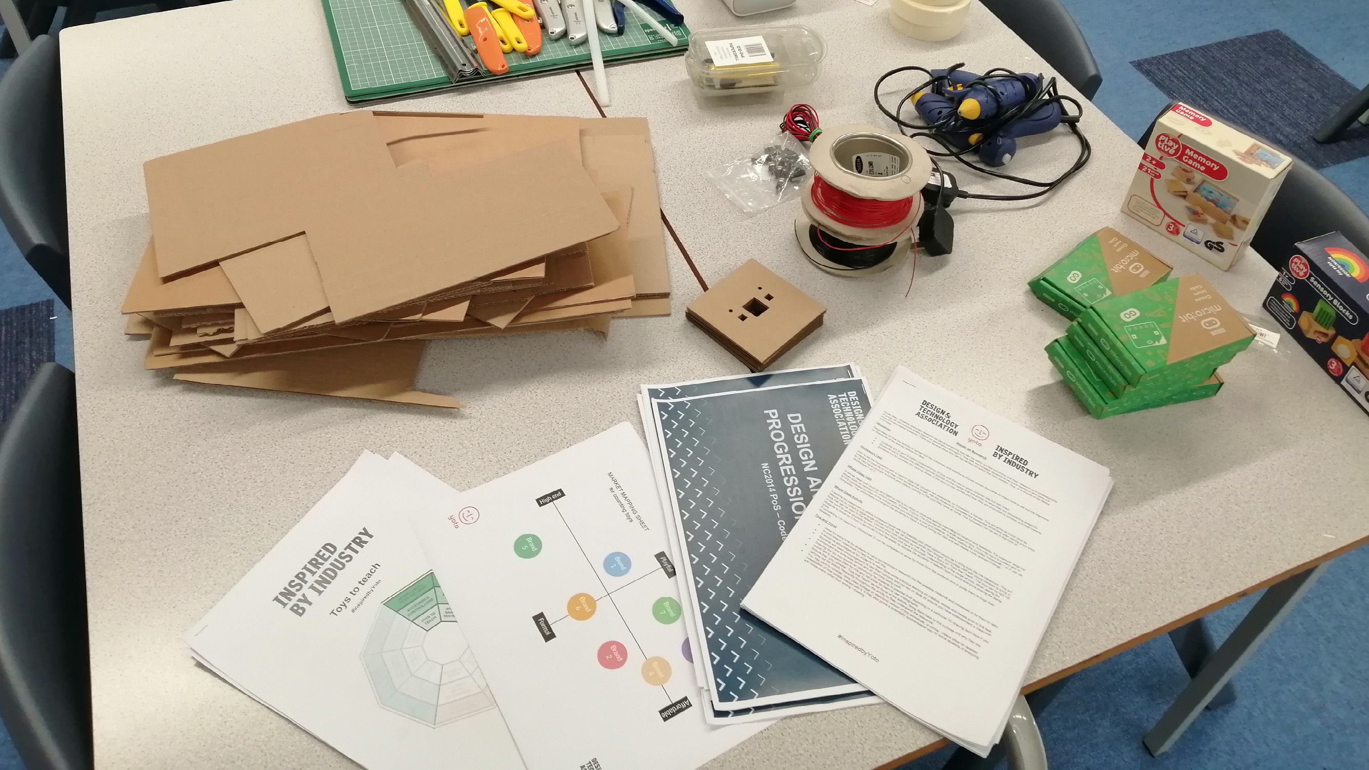 Table with cut cardboard, papers, micro:bits, wires and glue guns
