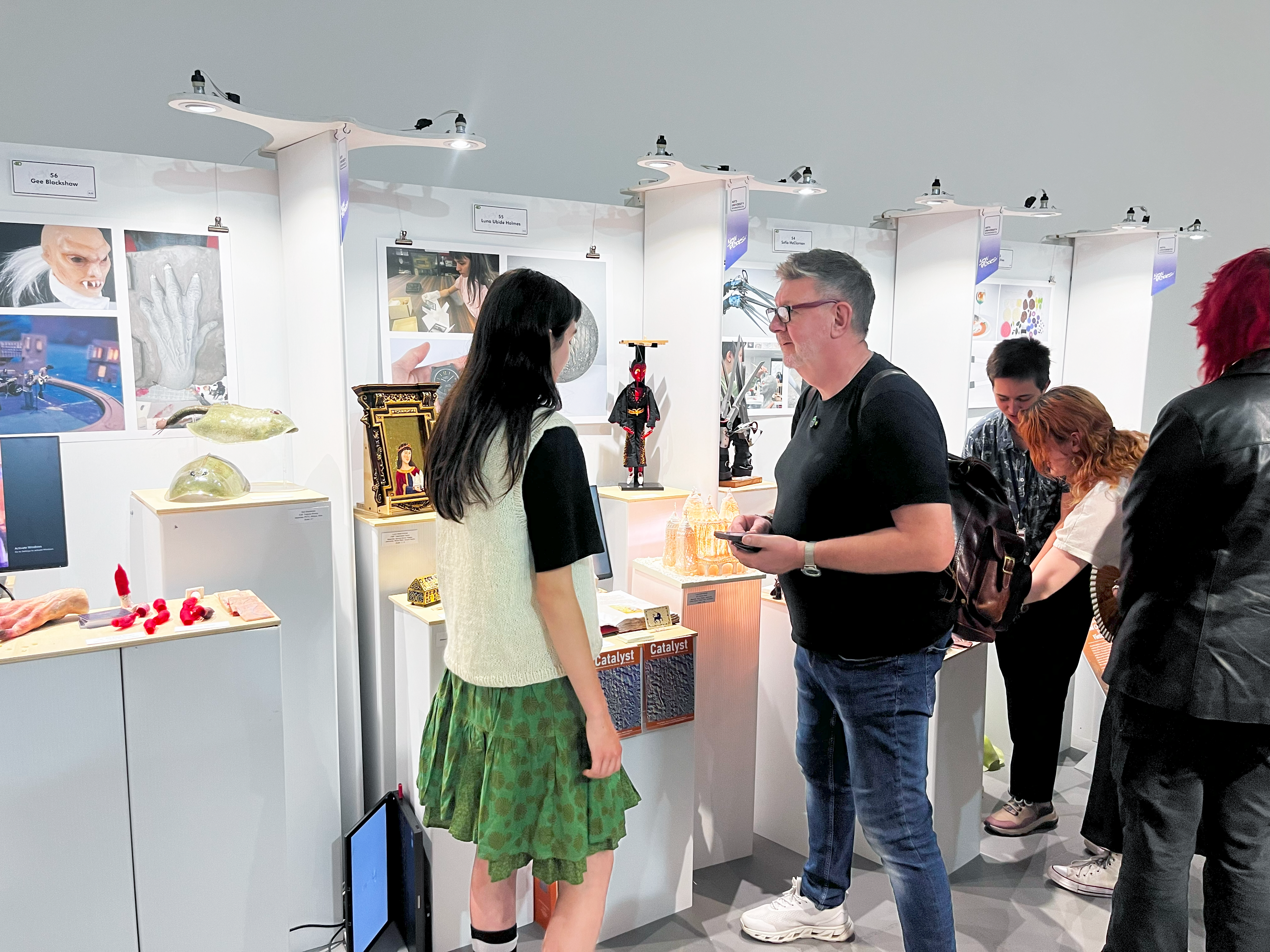 Visitors view and discuss student-designed artefacts displayed on plinths at a creative design and technology exhibition.