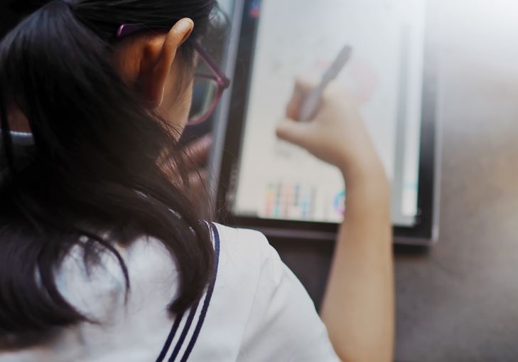 Student using a digital tablet and stylus to draw or write on screen.