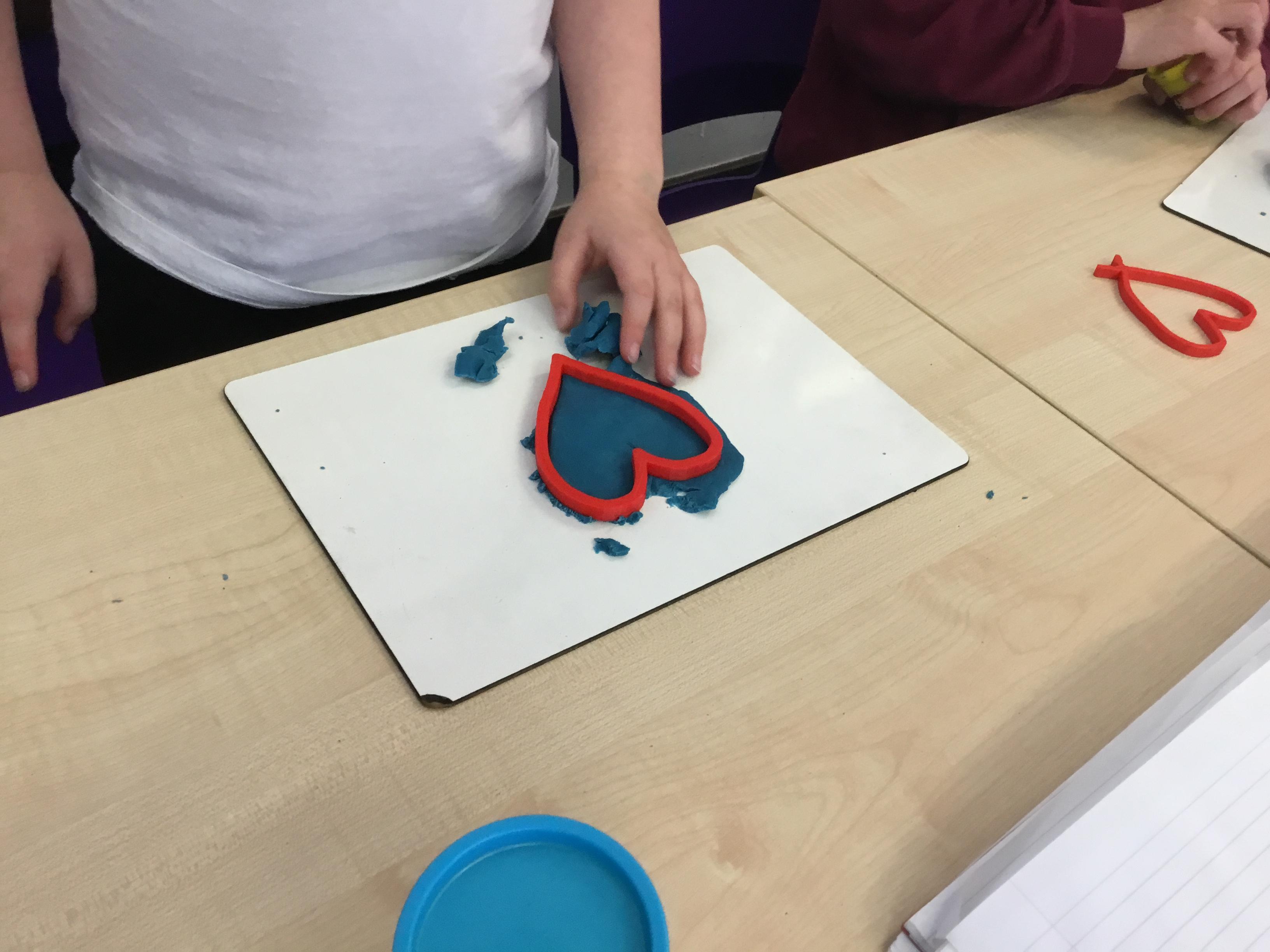A child using a 3D printed heart to cut a shape out of putty