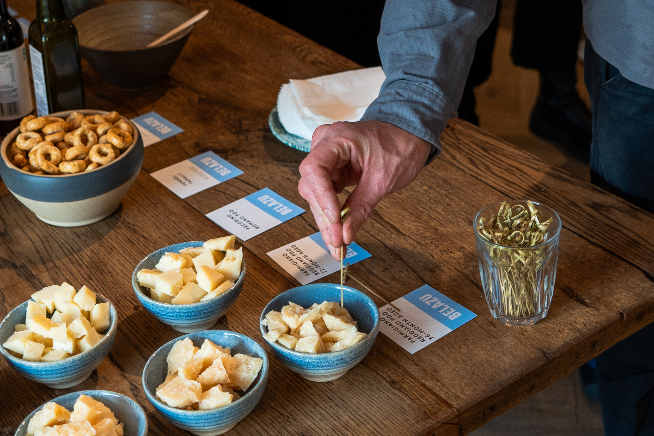 A display of Belazu olive oils, vinegars, and condiments arranged on a table with tasting bowls and product cards.