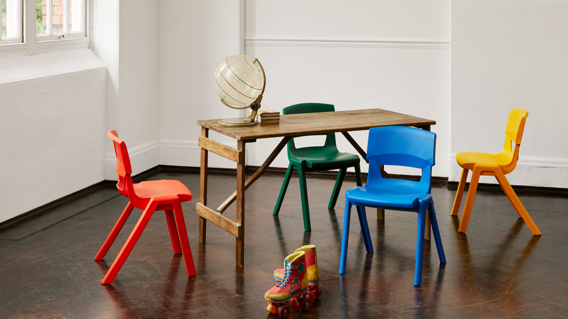 A classroom-style setting with a wooden table, colourful plastic chairs, and a globe, illustrating furniture design, ergonomics, and learning environments.