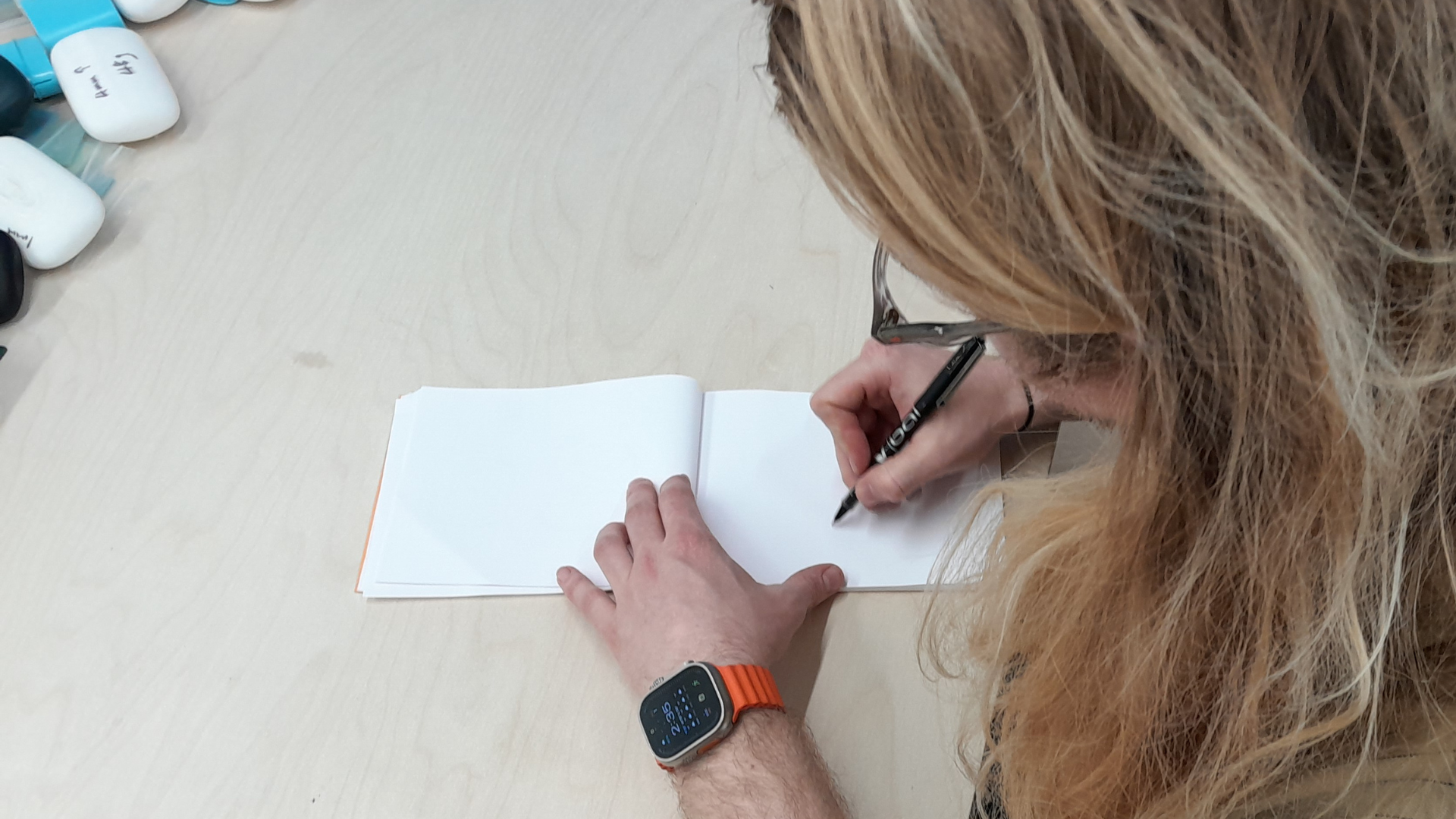Person sketching ideas in a notebook at a desk, showing hands drawing with a pen during an early design development activity.