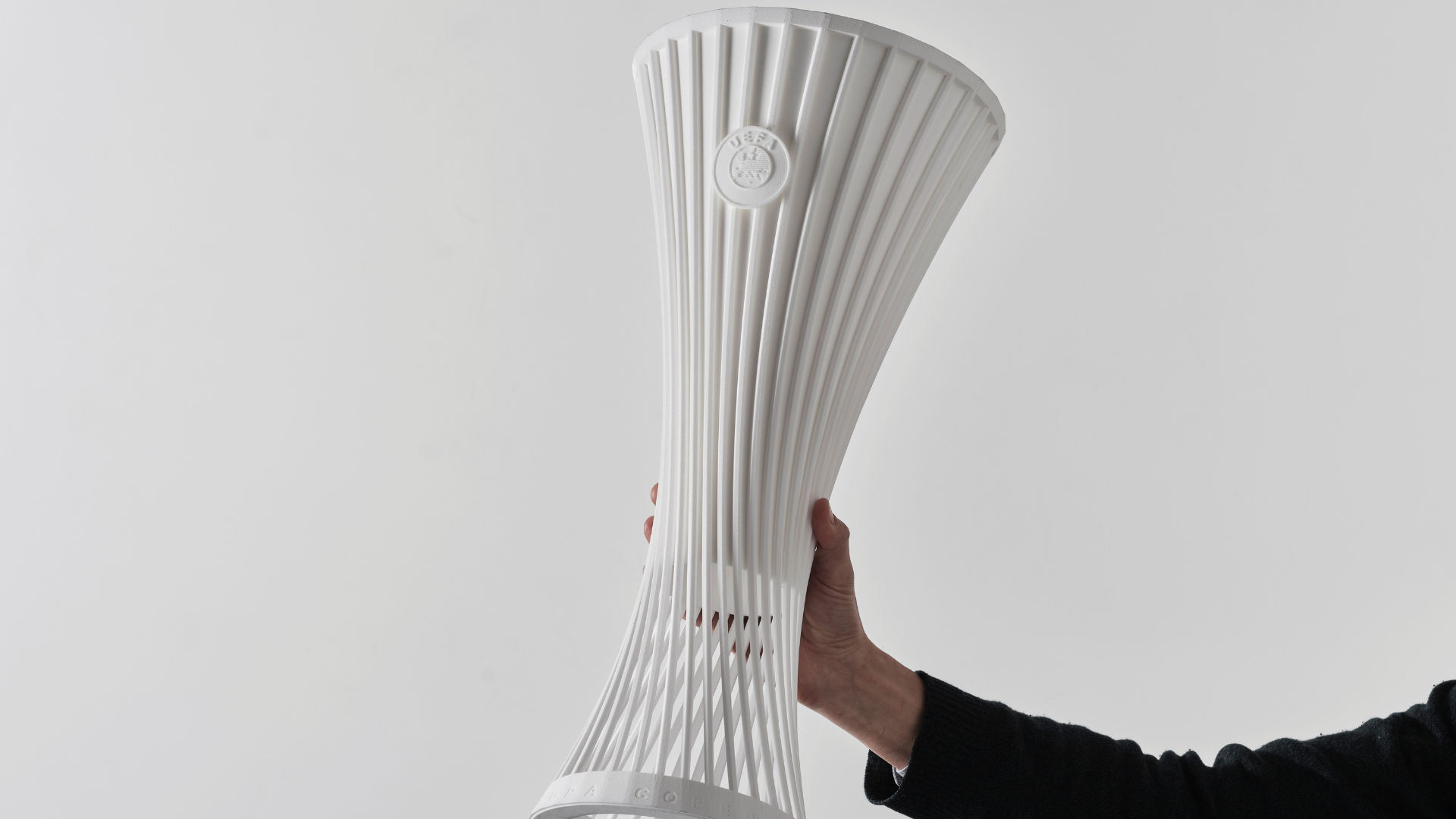 A hand holding a white 3D-printed trophy with vertical ribbed fins and a twisted, hourglass-like form against a plain background.