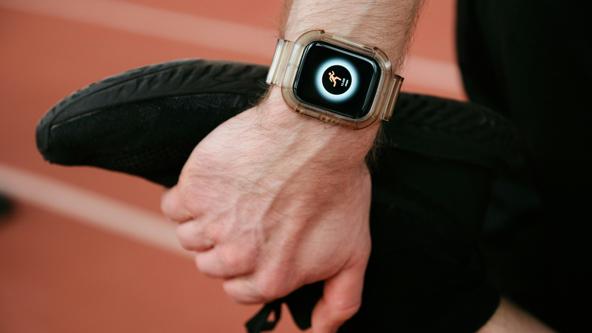 Athlete holding a shoe while wearing a smartwatch displaying fitness tracking data, illustrating wearable technology used to support sports performance.