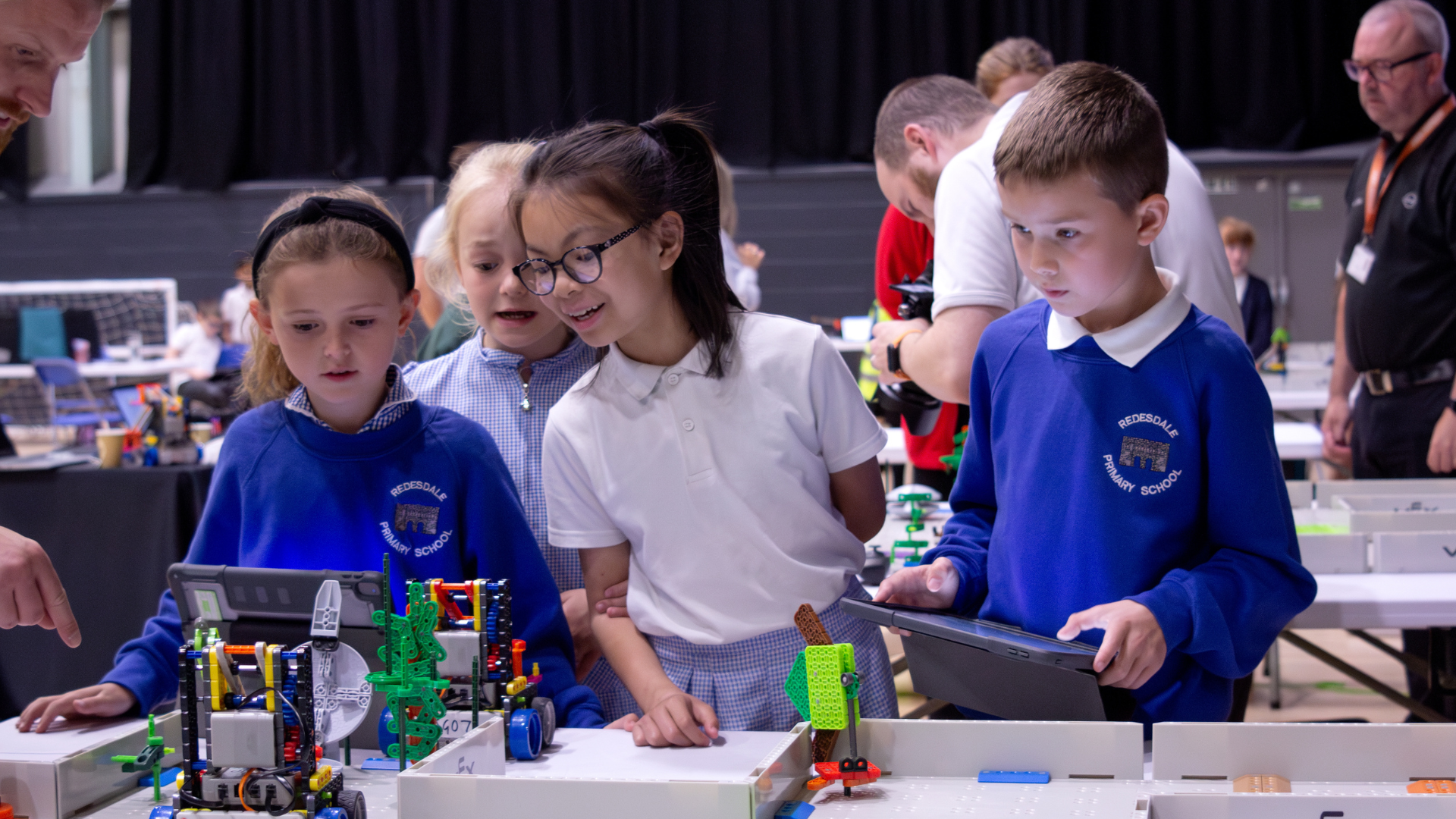 Primary school pupils working together on a hands-on design and technology activity using construction kits and tablets.