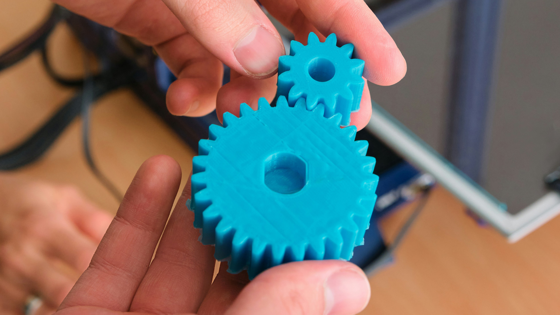 Close-up of two 3D-printed plastic gears being held, showing gear teeth and mechanical design.