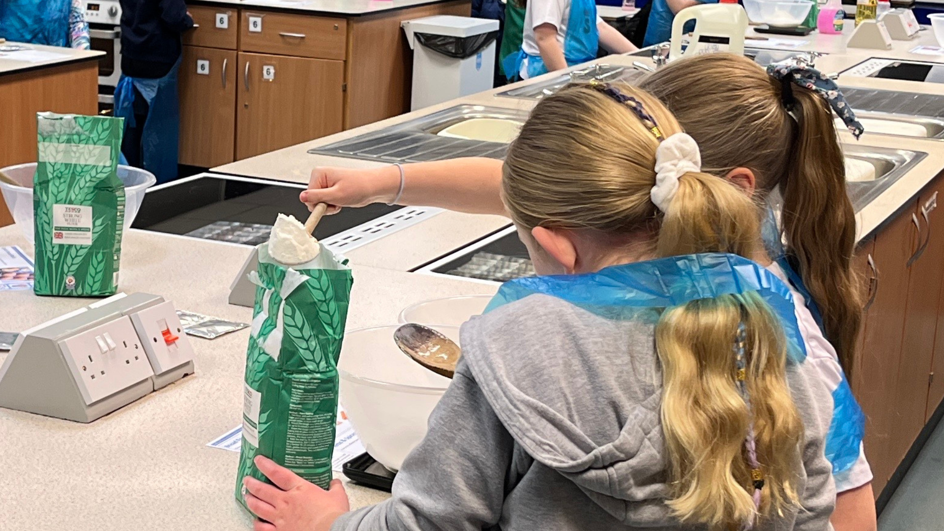 Primary school pupils measuring ingredients and mixing food in a design and technology kitchen classroom.