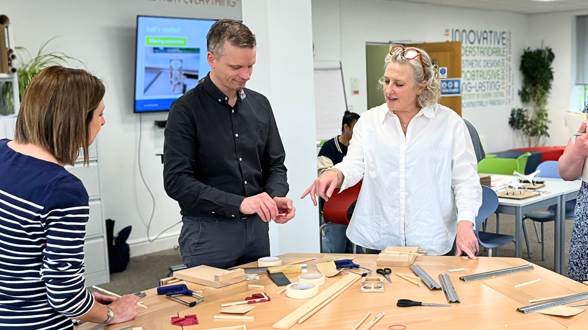 Teachers and educators working together around a table, exploring model-making tools, materials and small prototypes during a design and technology workshop.