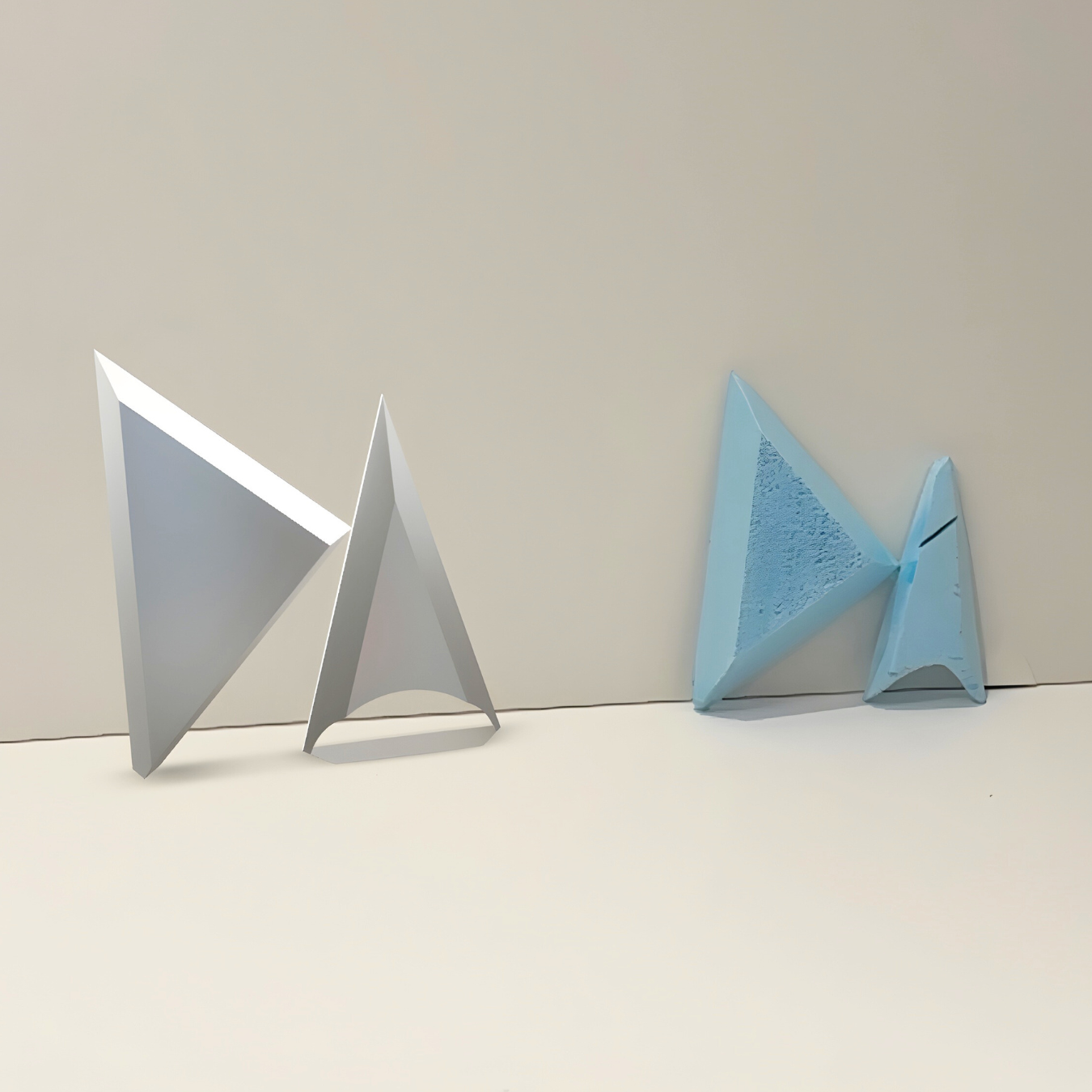 Two geometric trophy prototypes, one 3D printed in blue and one digital render in white, showing triangular forms and structural design