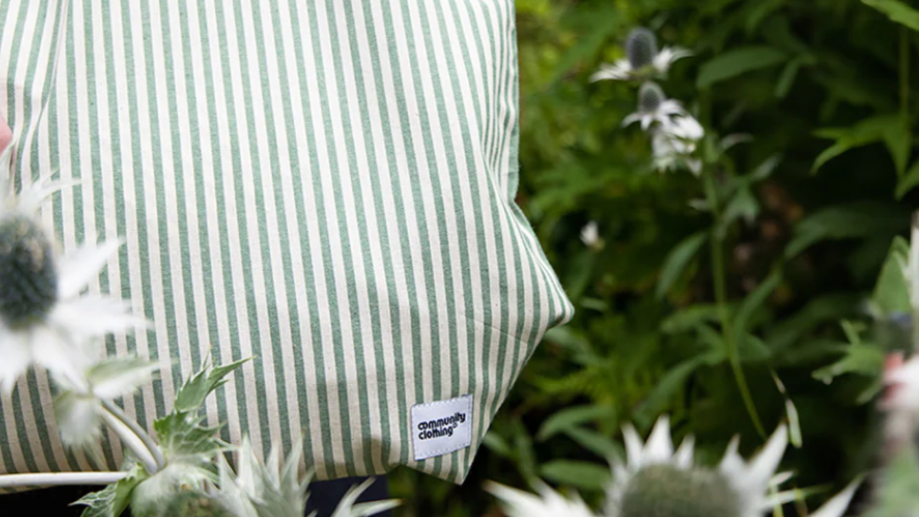 Green and white striped bag with a small fabric label, photographed outdoors among garden plants and flowers.