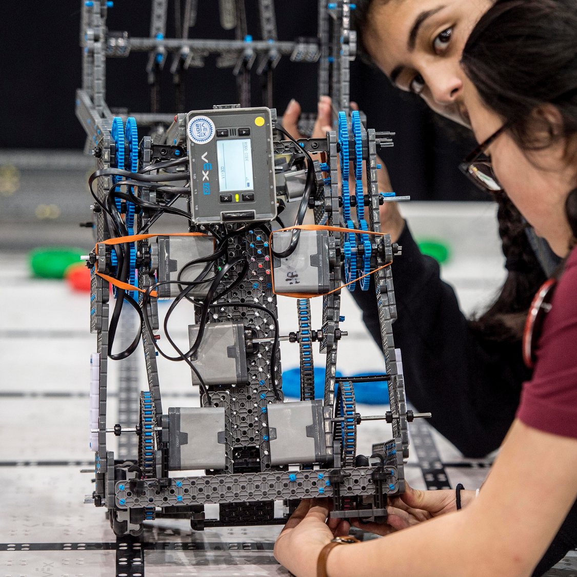 Students assembling and adjusting a VEX robotics system, working with gears, motors and a programmable control unit in a STEM classroom