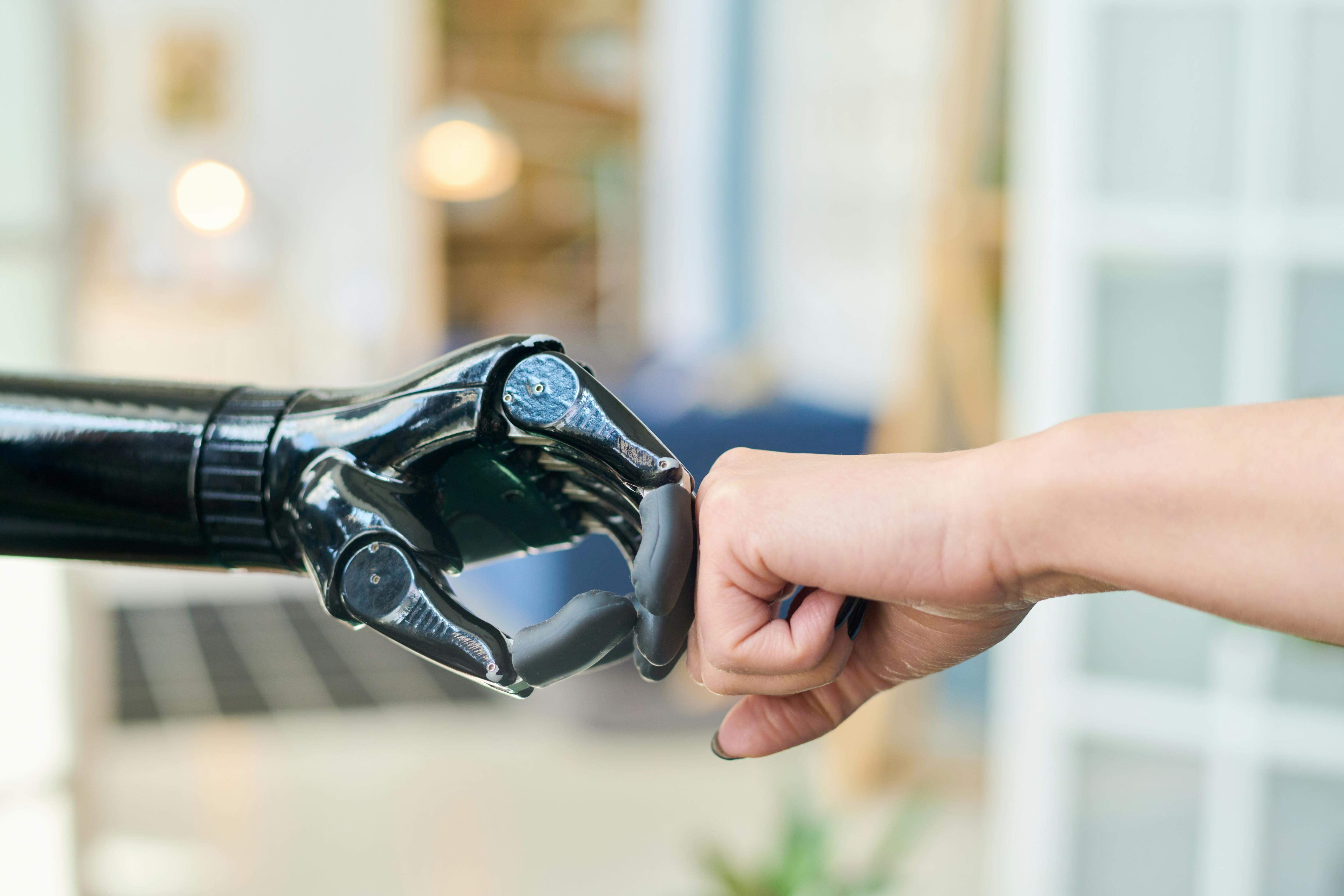 Close up of a robotic hand and a human fist touching, representing collaboration between people and artificial intelligence.
