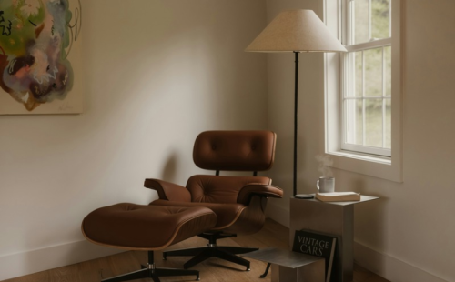 The image shows a brown leather Eames lounge chair with a matching ottoman, placed in an indoor room.
