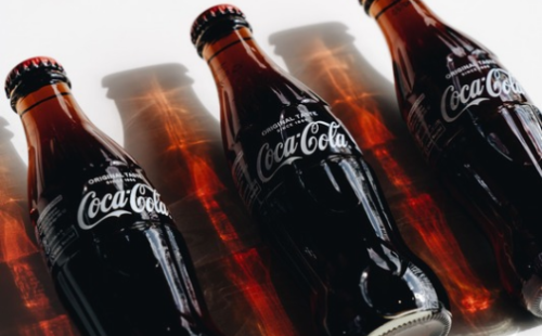 The image shows three Coca-Cola bottles lined up side by side on a white surface.