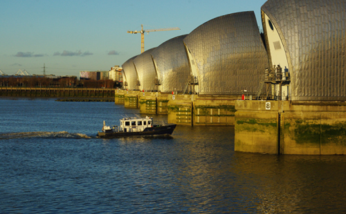 The image shows a boat traveling down a river approaching the Thames barrier.
