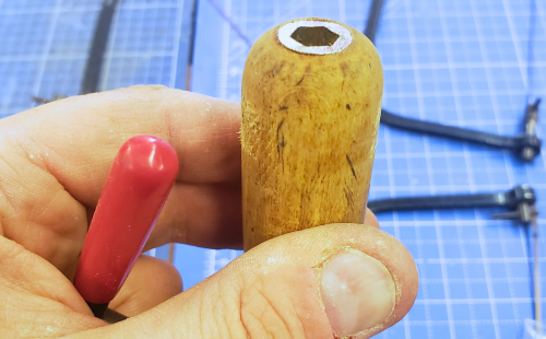 Close-up of a hand holding an adapted wooden tool handle in a workshop