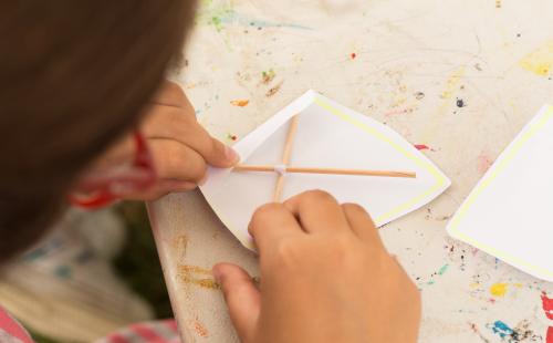 Child assembling a simple paper structure using wooden sticks