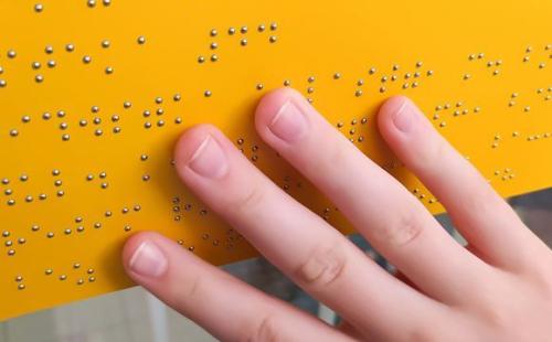 A hand reads raised braille dots on a yellow tactile sign.