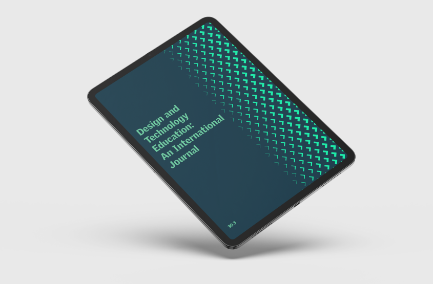 An image of a tablet displaying the cover of the journal Design and Technology Education: An International Journal, resting on a wooden desk next to a cup of coffee, wireless earbuds, and a pencil.