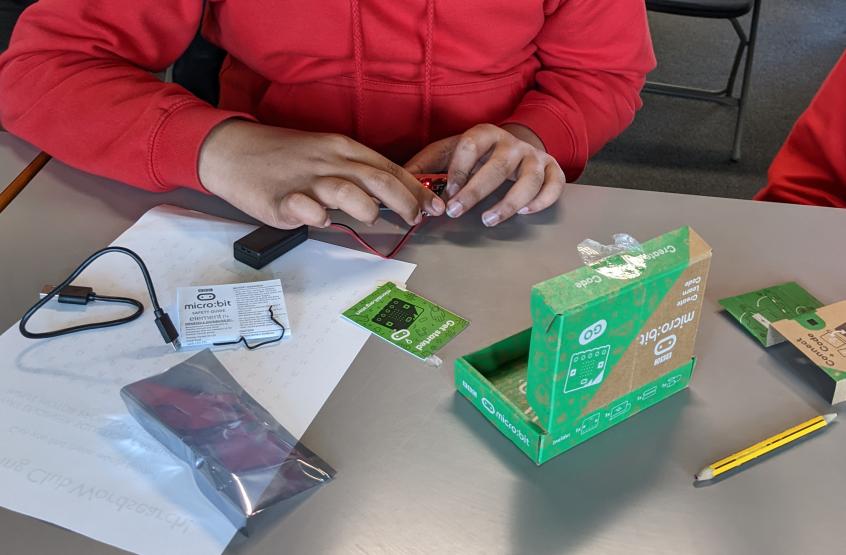 Student assembling a BBC micro:bit electronics kit in a classroom.