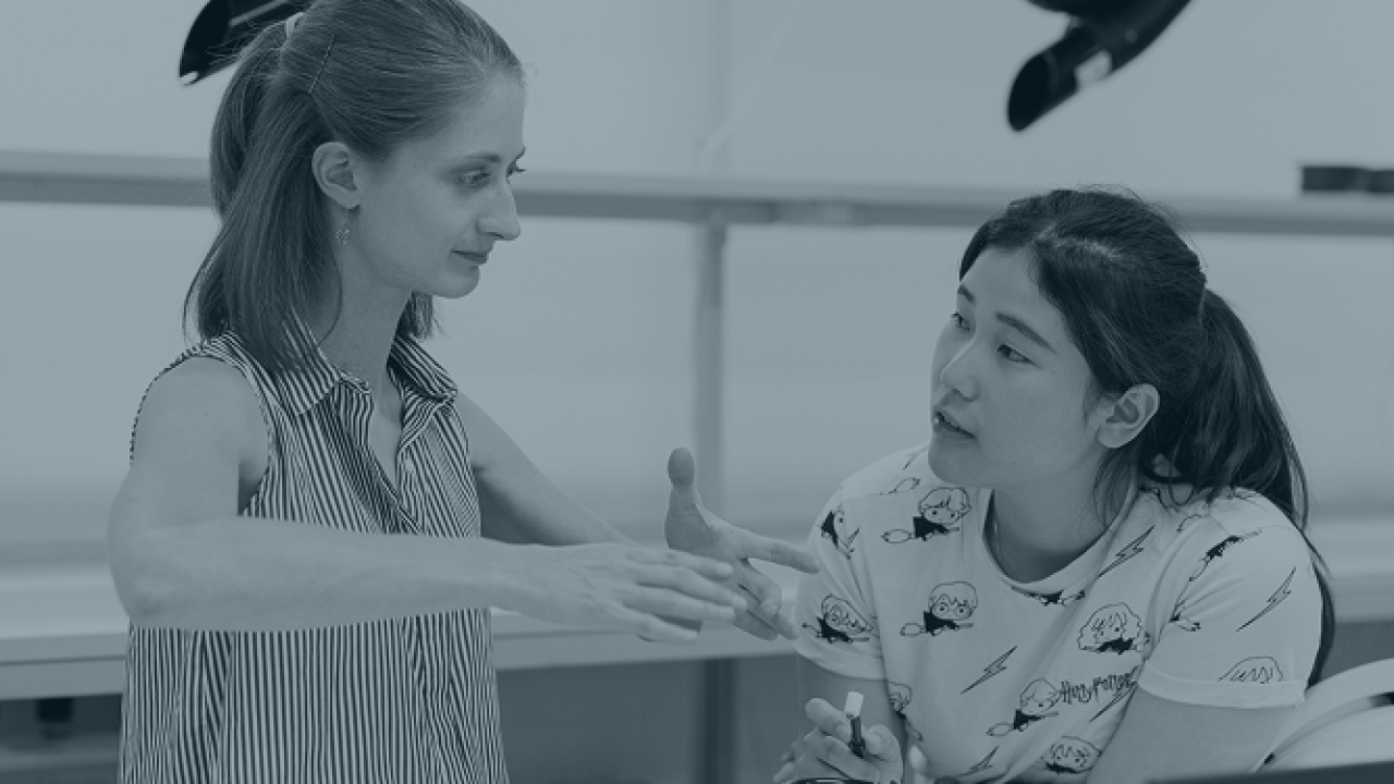 A teacher and student engaged in a focused discussion in a classroom or workshop setting.